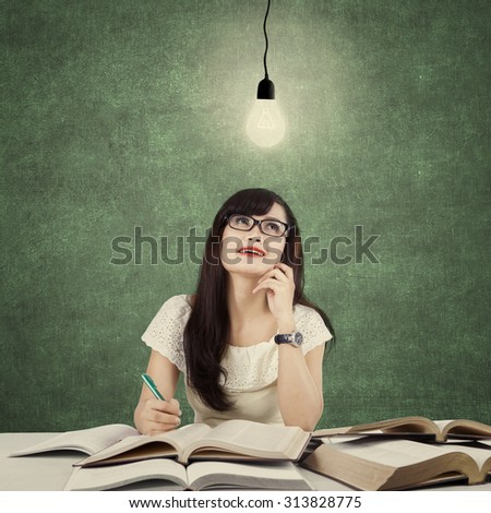 Photo of a clever college student studying in the classroom and get idea under bright light bulb