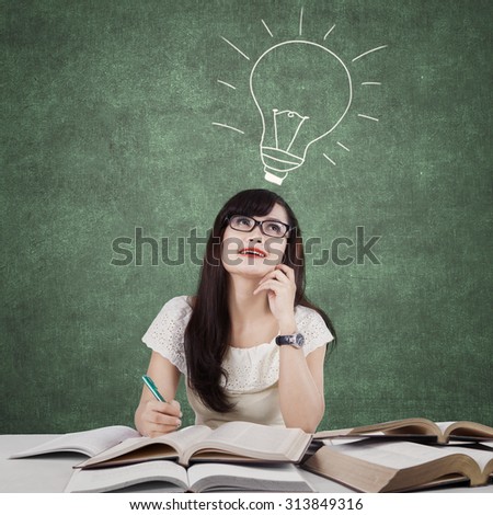 Photo of a creative female student doing school task in the classroom and get idea with a light bulb on the blackboard