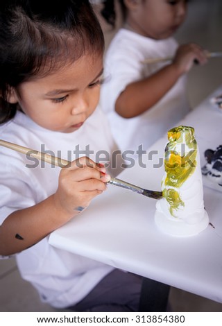 Child painting, little girl having fun to paint on stucco doll,selective focus on hand holding paintbrush