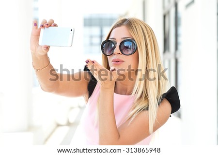 Beautiful woman, instagram. Woman taking a selfie with smart phone outdoors in the city on sunny summer day. Closeup shot. Cute girl with blond hair posing for self portrait