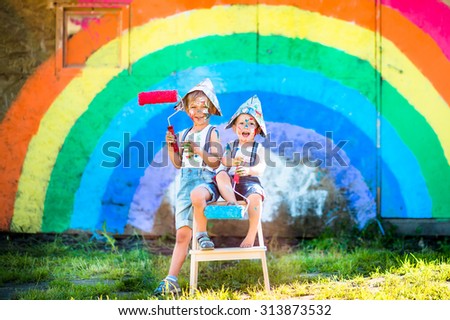 Two little boys with painted faces on a rainbow background hold paint rollers