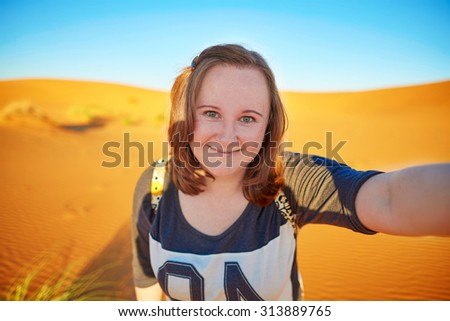 Happy smiling tourist taking selfie with sand dunes in Sahara desert, at Erg Chebby, Merzouga, Morocco