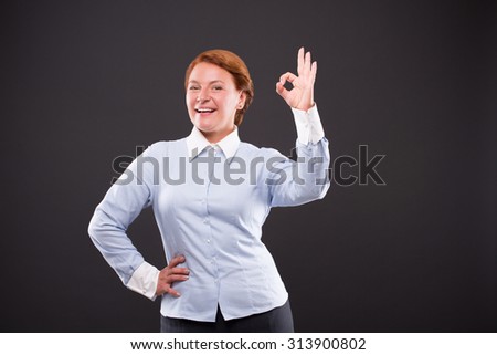 Smiling businesslady showing okay sign and keeping one hand on hip. Happy woman in blue shirt knows exactly that everything will be okay.