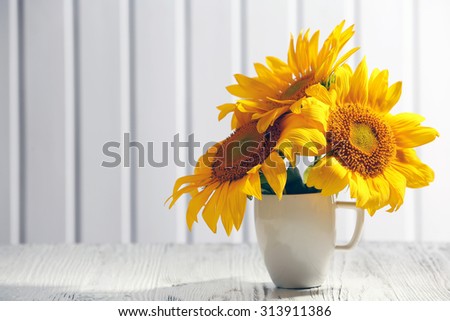 Beautiful bright sunflowers in cup on wooden background