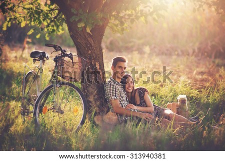Attractive Couple Enjoying Romantic Sunset Picnic in the Countryside / Vintage style photo with custom white balance, color filters, soft focus effect, and some fine film grain added