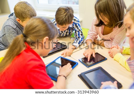 education, elementary school, learning, technology and people concept - group of school kids with tablet pc computer having fun and playing on break in classroom Royalty-Free Stock Photo #313943960