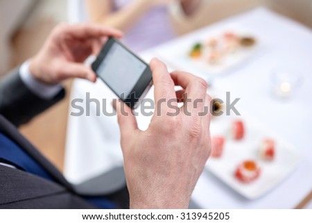 people, leisure, eating, food and technology concept - close up of couple with smartphones taking picture of sushi at restaurant