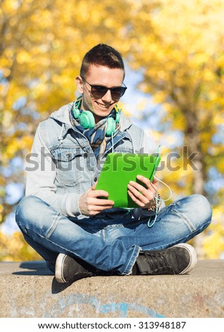 technology, lifestyle, season, music and people concept - smiling young man or teenage boy with tablet pc computer and headphones over autumn park background