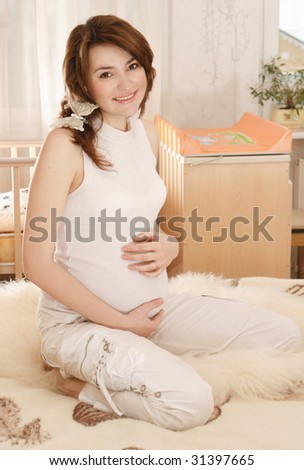 Happy pregnant woman in white clothes sitting in nursery

