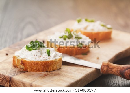 crunchy baguette slices with cream cheese and green onion on olive board, vintage toned