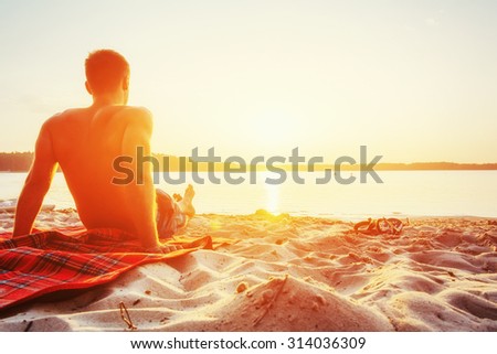 man sitting on the sand at sunset