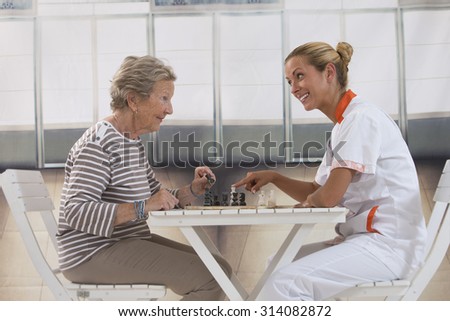 Senior woman playing chess with a nurse in a retirement home