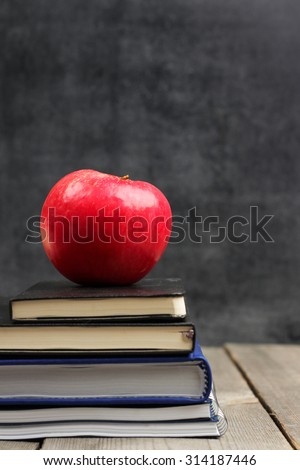 Still life, business, education concept. Notebook stack and apple on a wooden table with chalk and chalkboard. Selective focus, copy space, school background