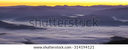 Foggy sunrise in the mountains.silhouettes tops of the mountains.above the clouds