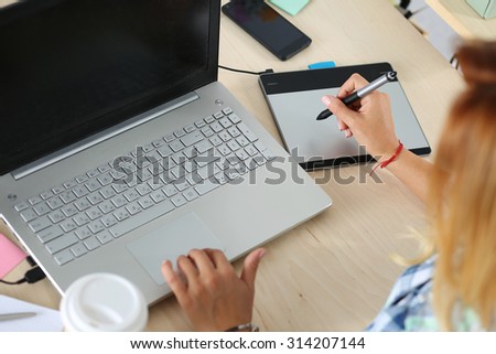 Hands of female designer in office working with digital graphic tablet and laptop. Photography retoucher sitting at desk and looking in display. Creative people or advertising business concept