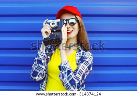 Fashion pretty cool girl wearing a colorful clothes with retro camera shooting over blue background