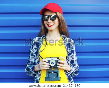 Fashion pretty smiling girl wearing a colorful clothes with retro camera over blue background