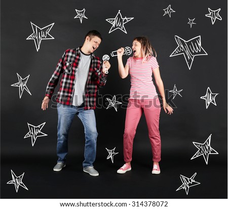 Funny young couple singing together with microphones, on black background