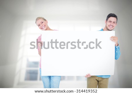 Smiling young couple holding a blank sign against room overlooking city