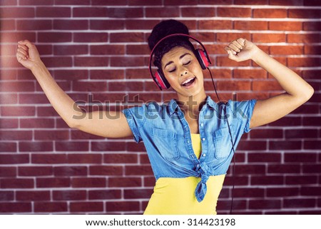 A smiling woman dancing with headphones on a brick wall