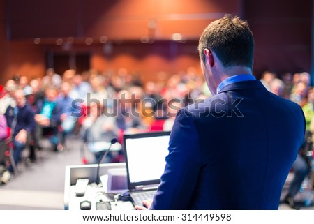 Speaker at Business Conference with Public Presentations. Audience at the conference hall. Entrepreneurship club. Rear view. Horizontal composition. Background blur. Royalty-Free Stock Photo #314449598