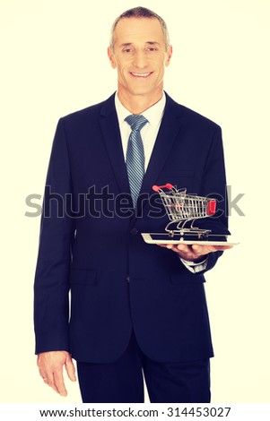 Businessman holding shopping cart on tablet.