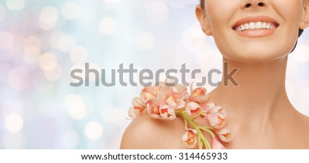 beauty, people and health concept - close up of smiling woman with orchid flower on her shoulder over blue lights background