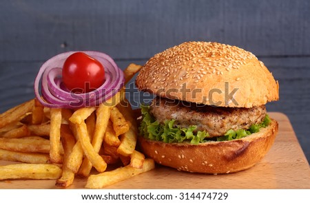 One big tasty appetizing fresh burger of green lettuce red tomato cheese bacon slice meat cutlet violet oinion and white bread bun with sesame seeds on wooden table closeup, horizontal picture