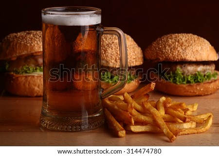 Three fresh tasty burgers of green lettuce meat cutlet cheese tomato and white bread bun with sesame seeds near chips and glass of dark beer on octoberfest holiday, horizontal picture