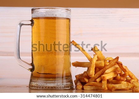 One big glass bocal of light cold delicious beer with white froth and tasty crispy yellow potato fasfood chips on wooden background closeup, horizontal picture