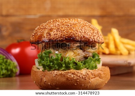 One big delicious fresh burger of green lettuce red tomato cheese meat cutlet violet onion and white bread bun with sesame seeds on wooden background closeup, horizontal picture