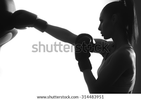 Side view of one strong concentrated female boxer with ponytail in boxing gloves training punching standing in studio on white background black and white copyspace, horizontal picture