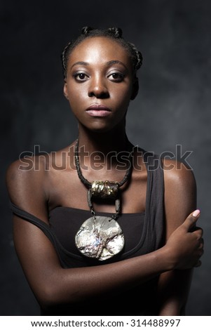 the proud black woman with an ethnic ceramic brilliant necklace surely looks in the camera. Studio photo against a dark background