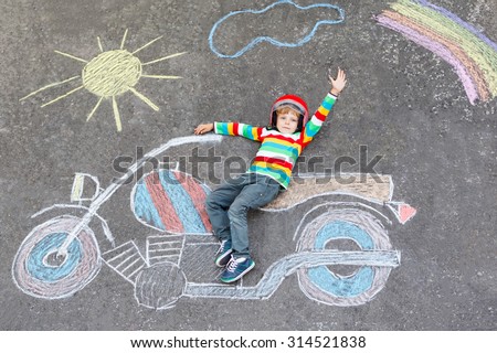 Creative leisure for children: Adorable little child of four years in helmet having fun with motorcycle picture drawing with colorful chalks. Children, lifestyle, fun concept.