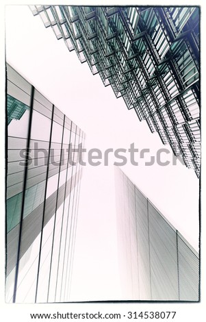 An abstract coloured photo looking up capturing three different buildings on a 45 degree angle with an applied cross process filter. Image has a film coated and vintage black border
