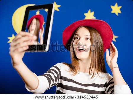 Picture of young woman trying on red hat and making selfie. Happy girl excited on stars and moon wallpaper background.
