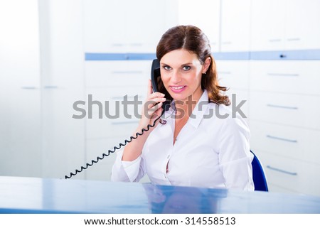 Doctors nurse with telephone in front desk making appointment with patient