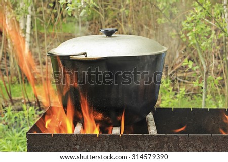 Tourist boiler with food standing on the grill over the fire. Focus on the pot.