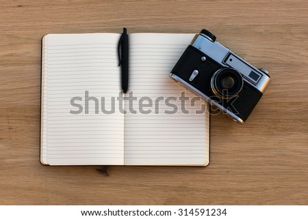 Open notebook with a pen and a vintage film camera, top view on wooden texture of the table.