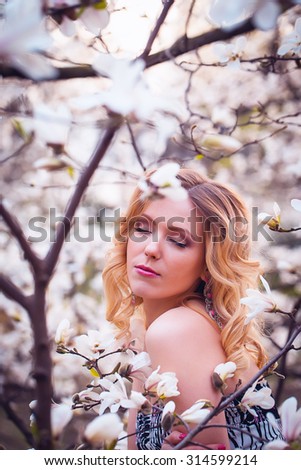 Beauty smiling woman near white magnolia in botanical garden