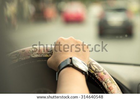 Image of a woman driving with hand on steering wheel on the road with selective focused point