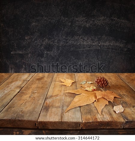 autumn background of fallen leaves over wooden table and blackboard background with room for text