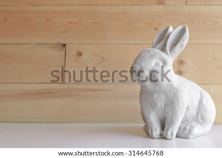 Sculpture of a Realistic White Rabbit as Interior Decoration Against Blur Wooden Background, for Wallpaper [Original Collection]