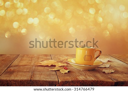 front image of coffee cup over wooden table and autumn leaves in front of autumnal sunset background 