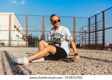 Close-up young boy relaxed and sitting on the grass and listen music on earphones,in sun reflecting bright sunglasses,denim tshirt.smiles and laughs,mans fashion style.teen fashion
