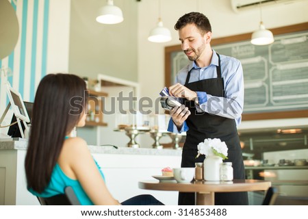 Attractive young waiter swiping a customer's credit card in a bank terminal at a cake shop