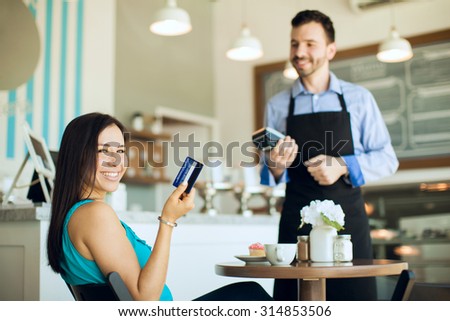 Portrait of a happy young Hispanic woman showing her credit card after using it at a coffee shop