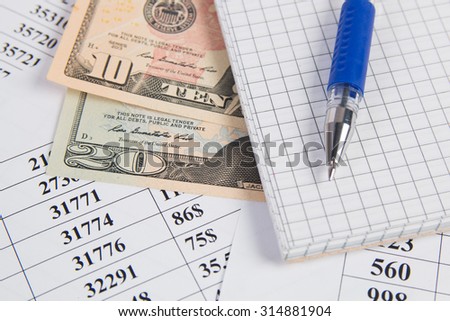 pen, notebook  and USA dollar bills on table with figures