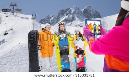 winter sport, technology, leisure, friendship and people concept - happy friends with snowboards and tablet pc computer taking picture over snow and mountain background