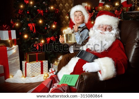 Santa Claus and laughing cute boy sitting in Christmas room with gifts. Christmas home dÃ©cor. 
